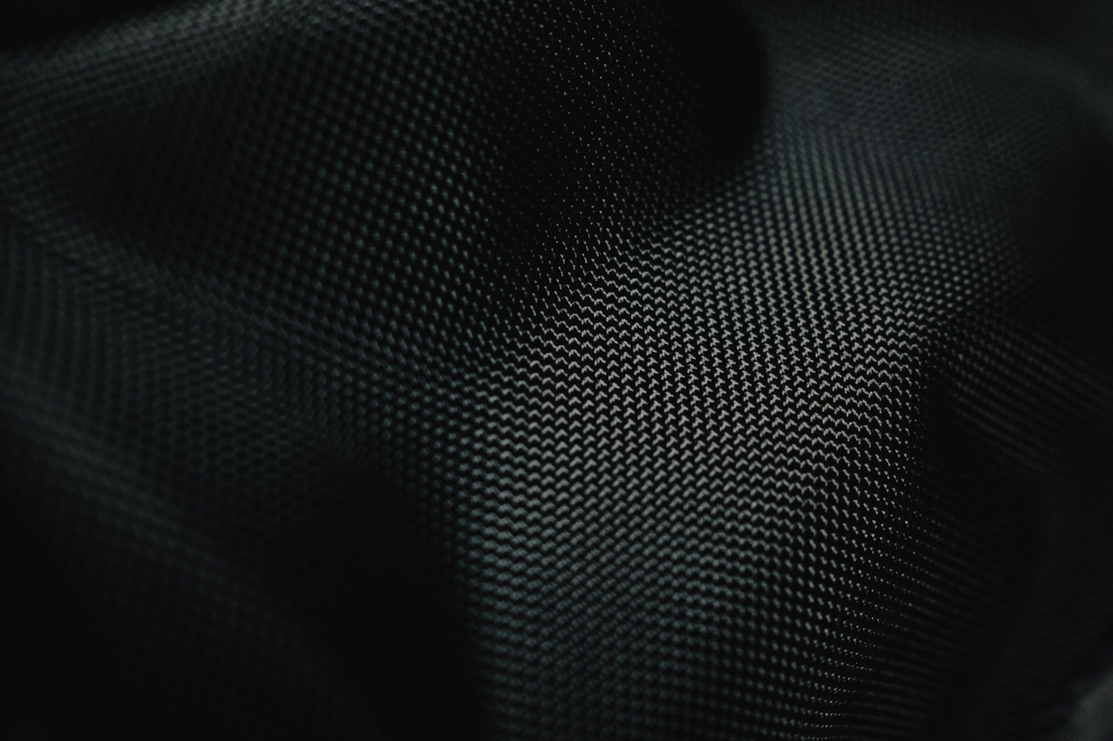 Raking light across the weave and drape folds of black technical fabric